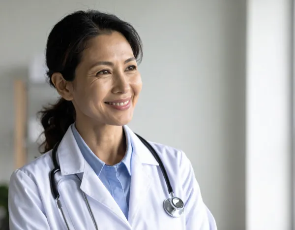 female doctor with gray hair wearing a white lab coat sitting at a table and smiling at a patient off camera