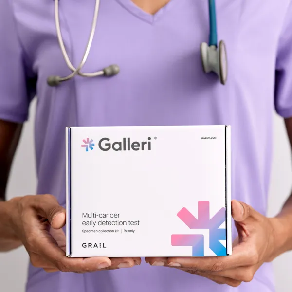 close up image of a person wearing purple scrubs and a stethoscope holding the Galleri test box