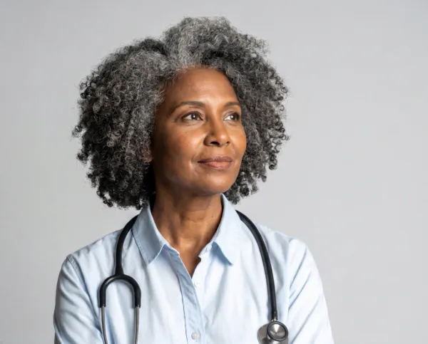waist up studio portrait of a woman in blue t-shirt with gray hair wearing a stethoscope gazing off camera