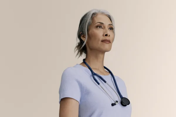 waist up studio portrait of a woman in blue t-shirt with gray hair wearing a stethoscope gazing off camera