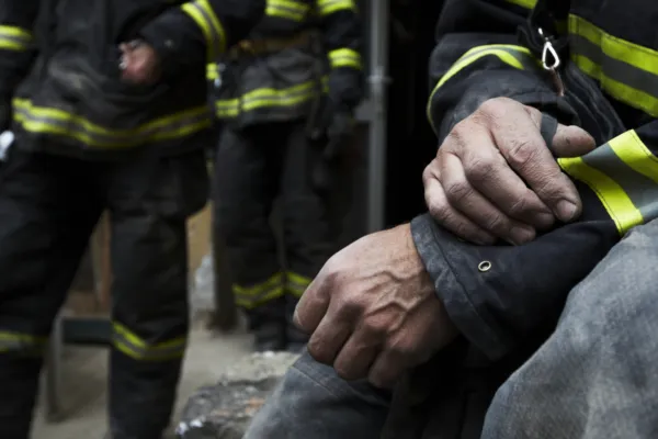close up of a firefighter's hands with other firefighters visible in the background